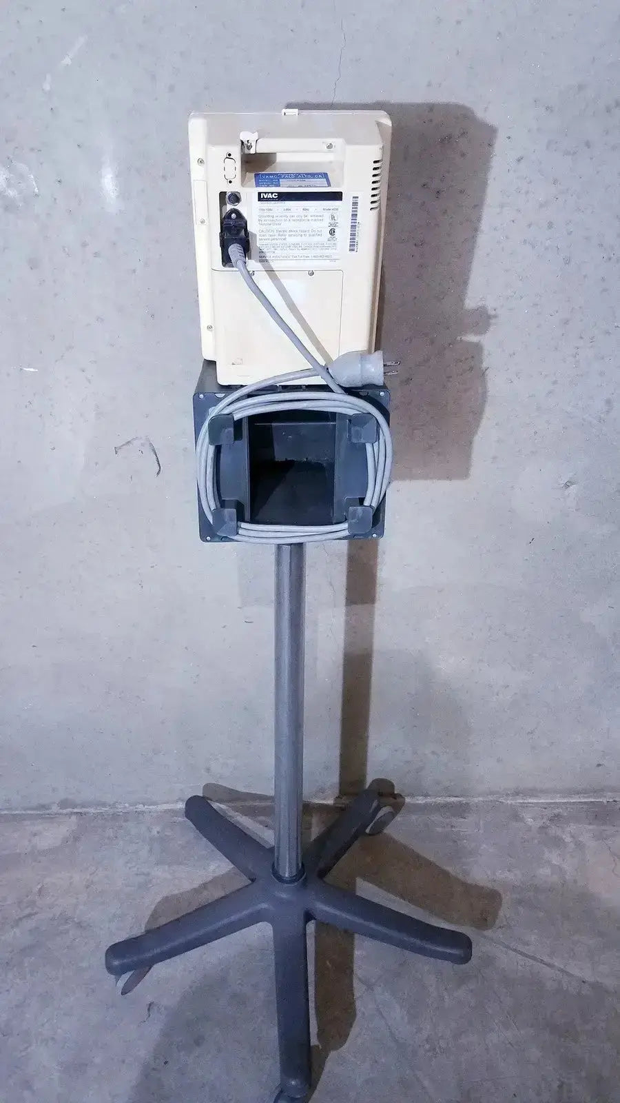 Cream-colored ivac corporation vital check 4200 medical device mounted on a gray adjustable stand with star-shaped base