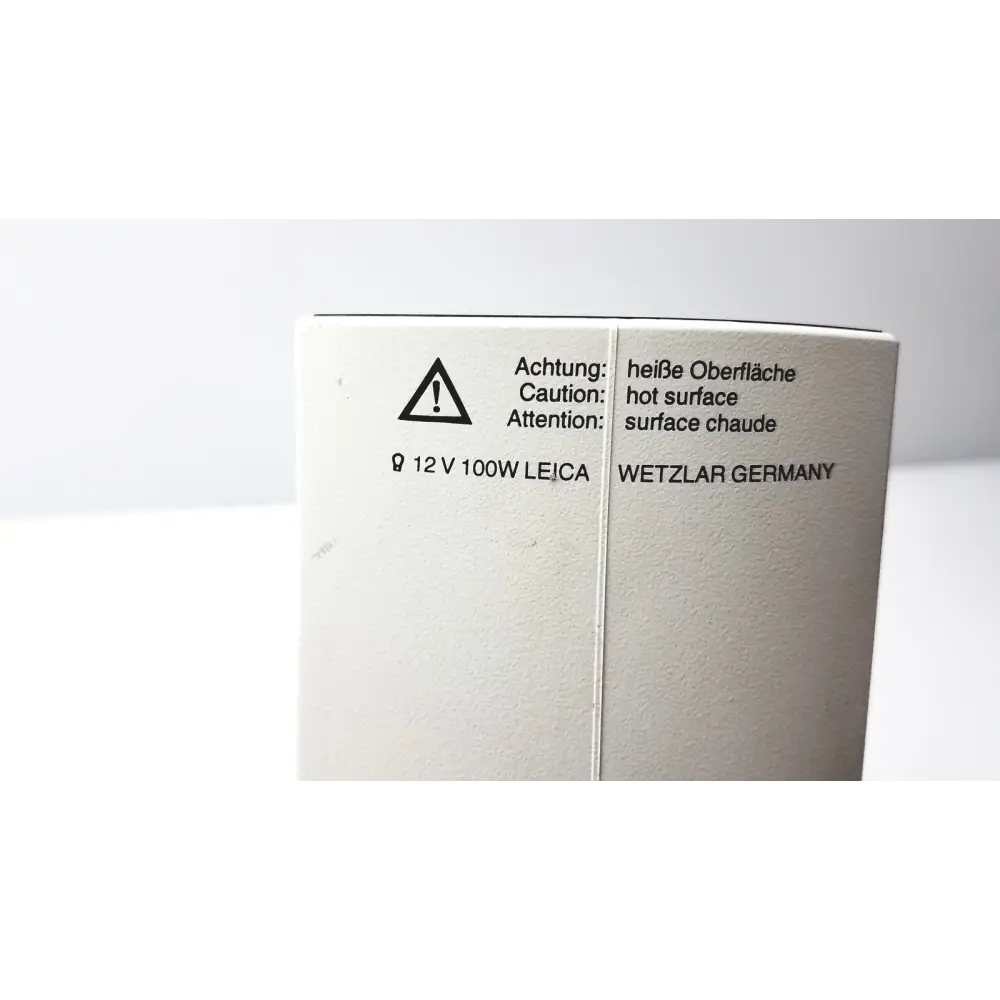 White cardboard box with black printed text and symbols, including a warning triangle for hot surface, voltage specification (12 v 100w), brand name ’leica,’ and location ’wetzlar germany.’