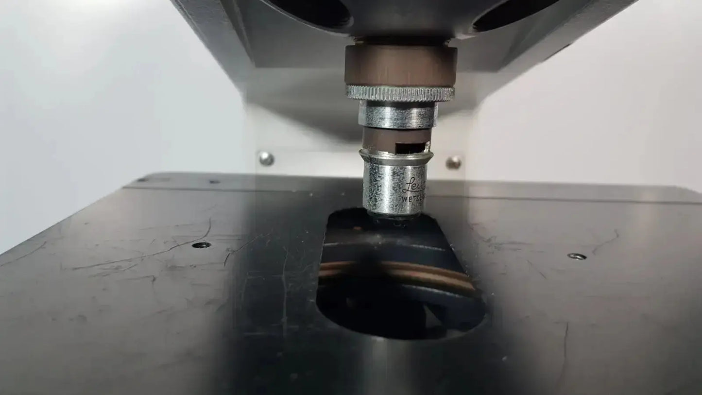 Silver-colored metal press tool with threaded collar and markings above dark metallic workpiece used with leitz metallux stereo zoom microscope