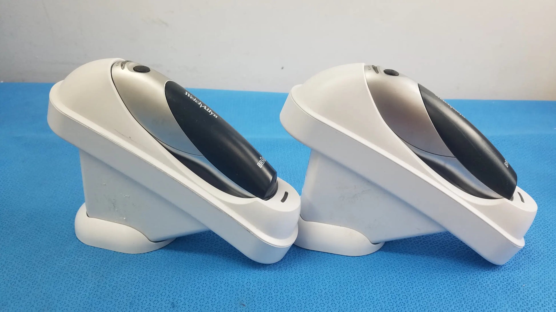 Two white and black handheld barcode scanners with silver accents resting in matching charging stands for reuse medical equipment