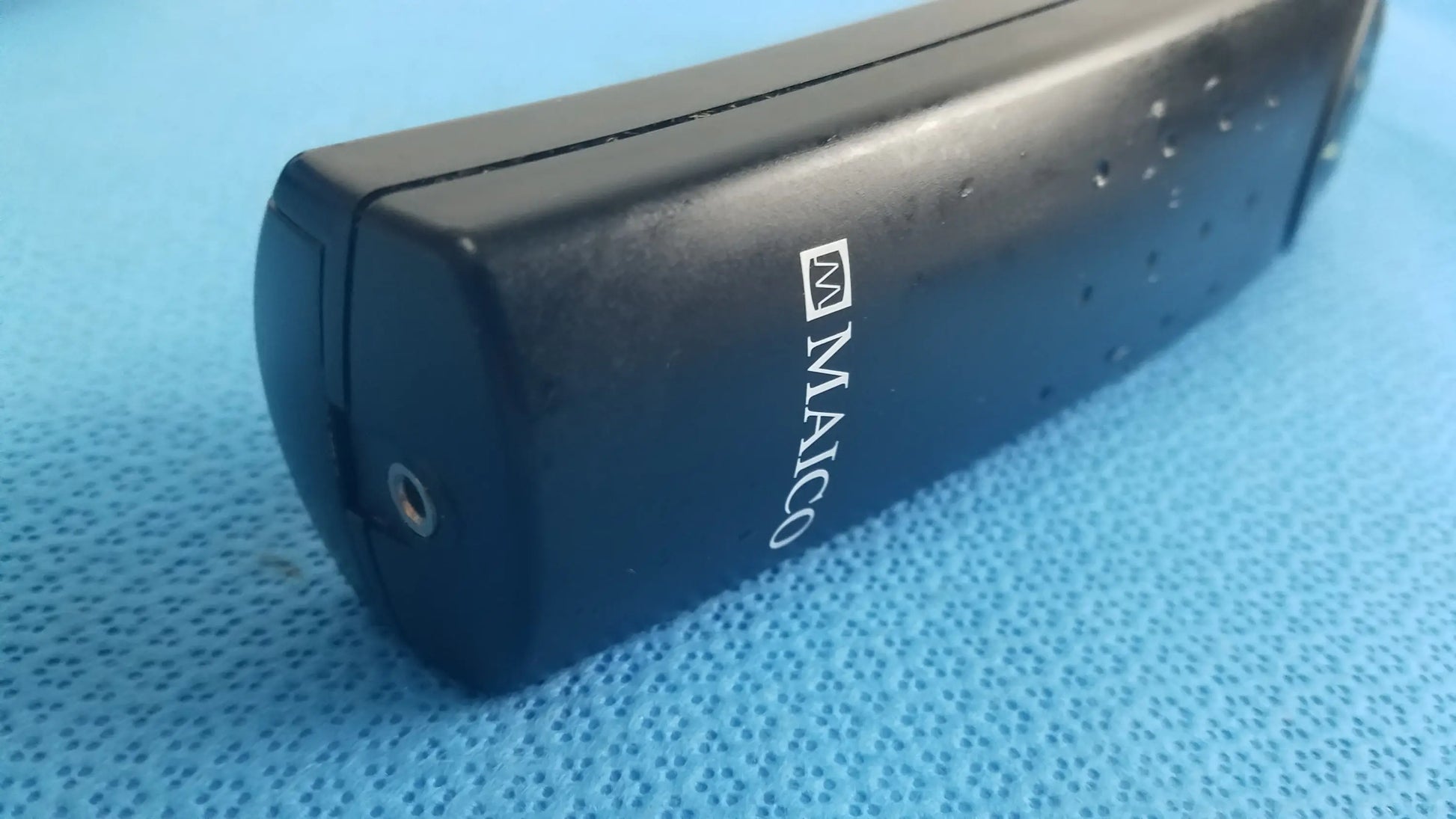 Black maico branded portable charger with matte finish and side perforations for handheld auditory medical equipment