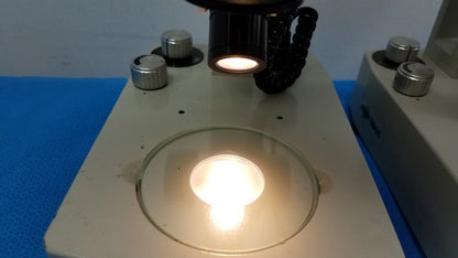 A circular glass slide on a beige microscope stage illuminated in meiji techno stereo microscope medical equipment