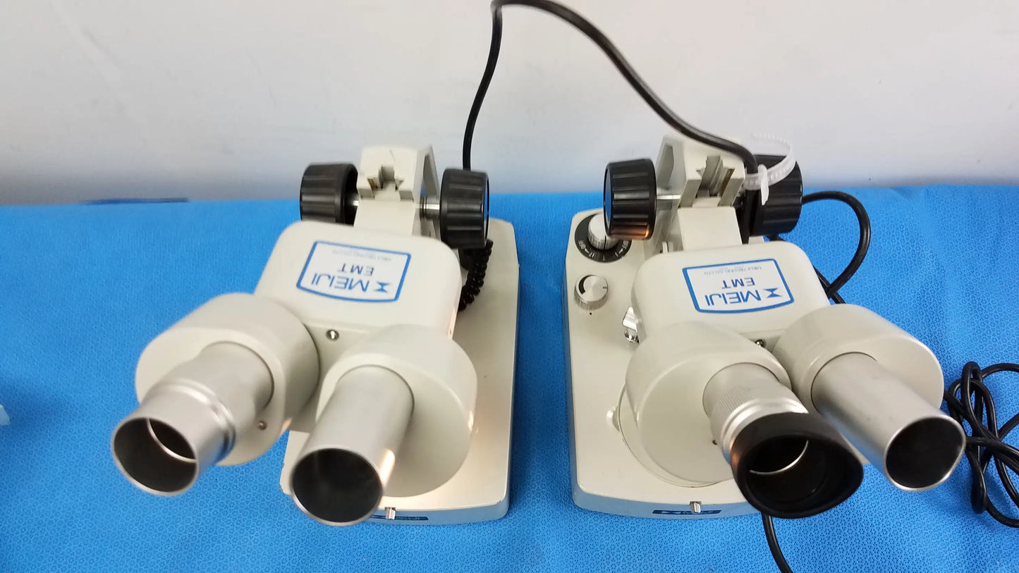 Two beige and silver meiji techno emt-1 stereo microscopes with black knobs on blue surface medical equipment