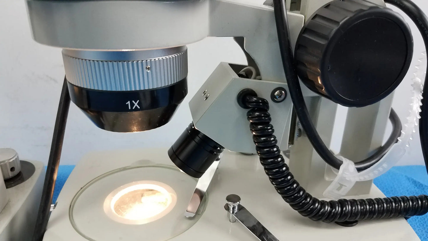 White and black meiji techno stereo microscope with 1x objective lens metallic parts and coiled cables medical equipment