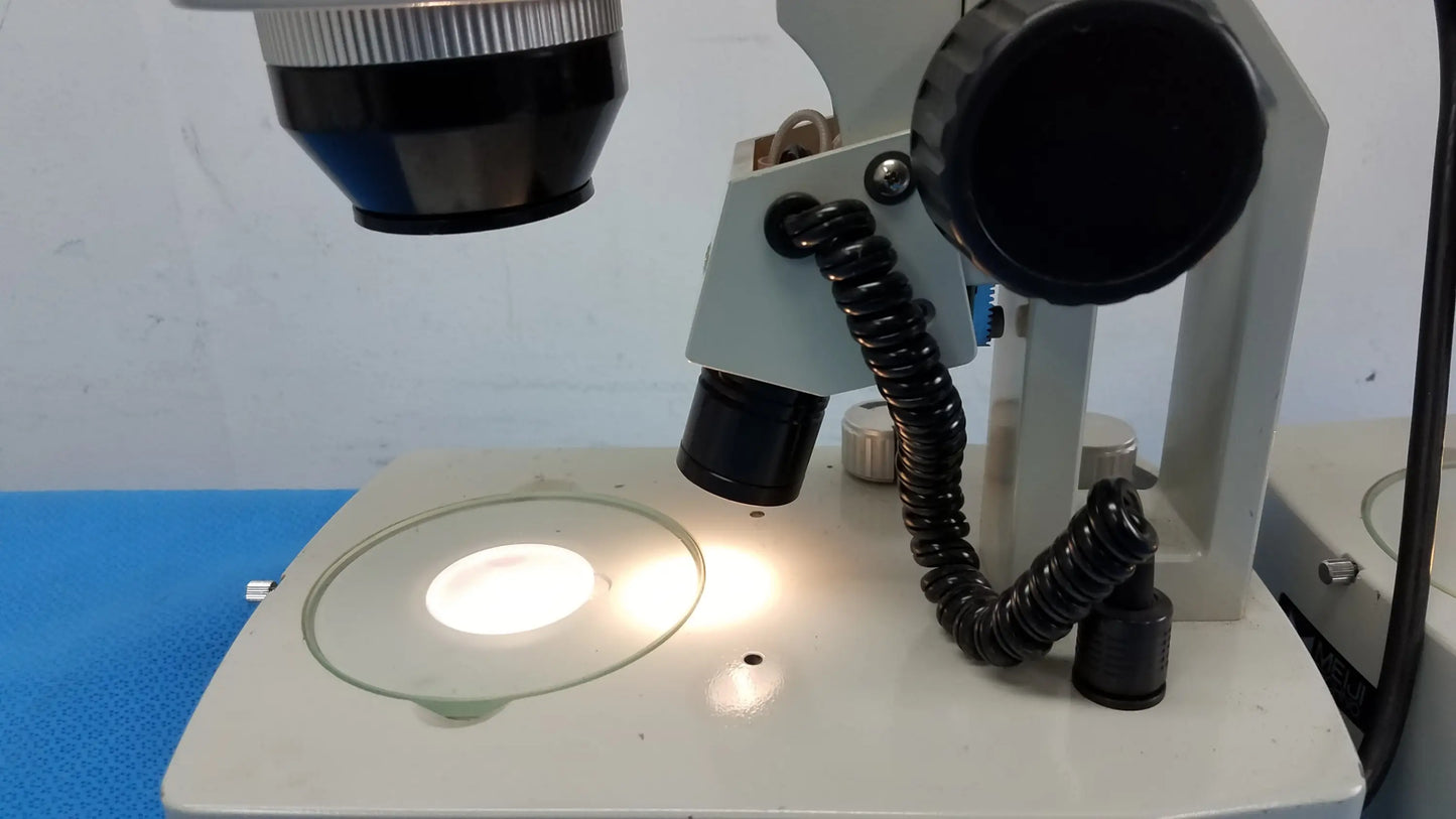 A white meiji techno stereo microscope with black eyepieces and circular stage light, essential medical equipment