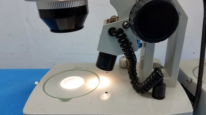 A white meiji techno stereo microscope with black eyepieces and circular stage light, essential medical equipment
