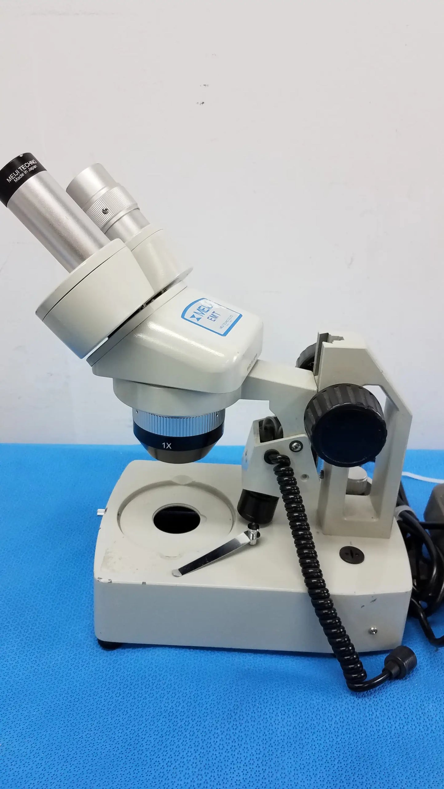 Beige inverted binocular microscope with silver eyepieces, black coiled cable, adjustable focus, and illuminated stage in stereo microscope set