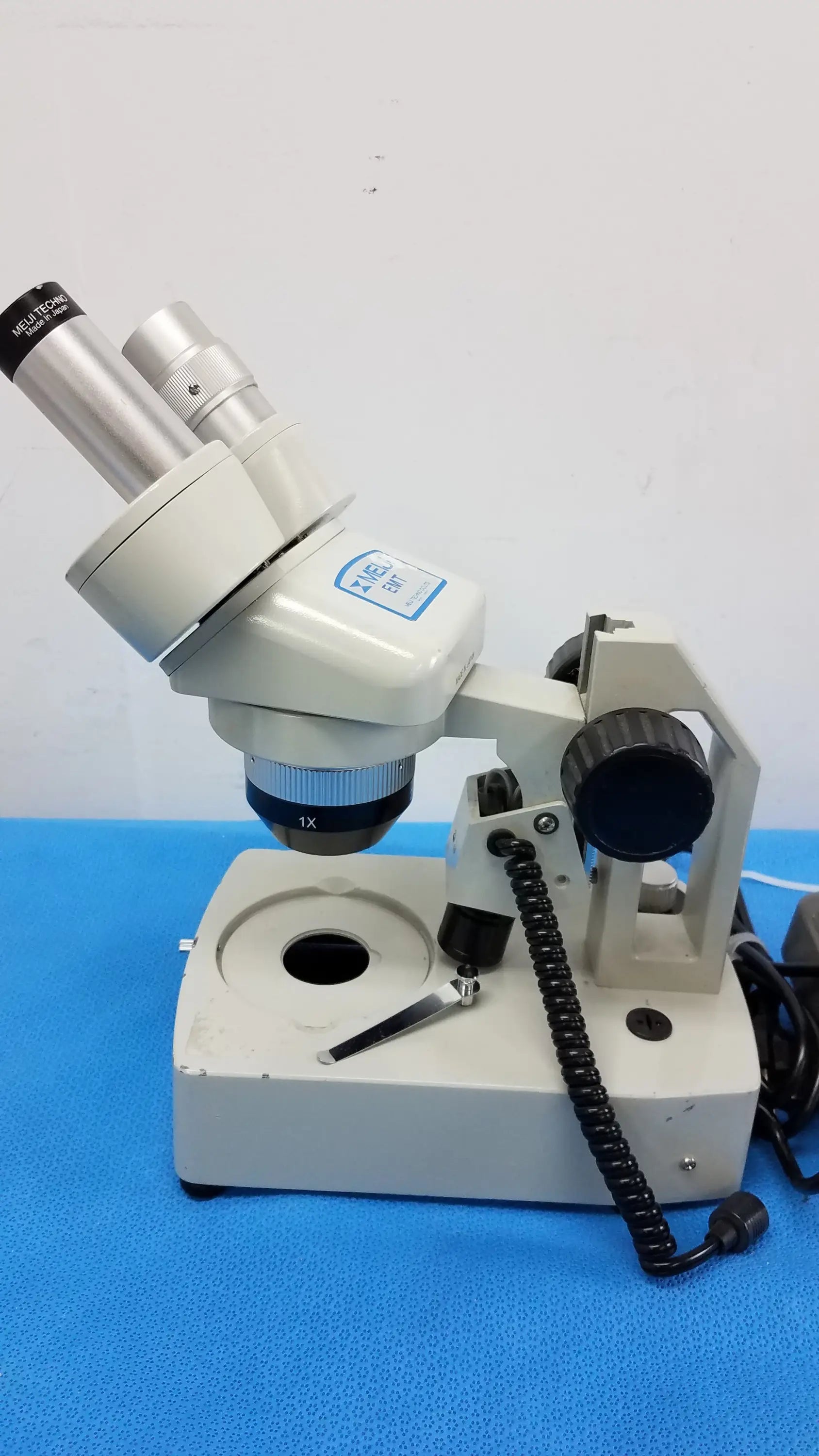 Beige inverted binocular microscope with silver eyepieces, black coiled cable, adjustable focus, and illuminated stage in stereo microscope set