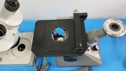 Black stage with circular opening and silver metallic parts on a gray base of an inverted binocular stereo microscope