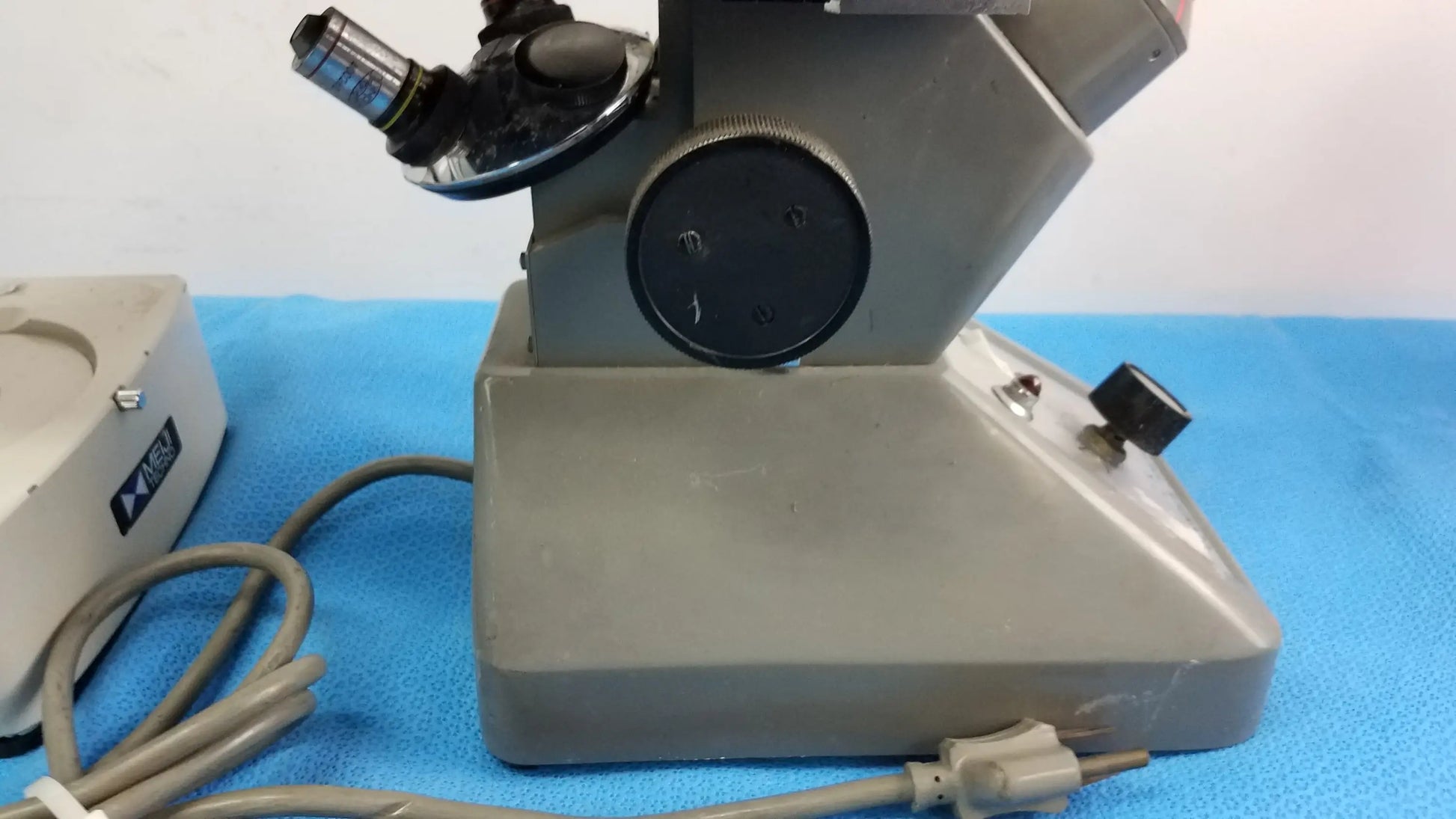 Gray metallic stereo microscope with black stage controls and silver-tipped objective lens for inverted binocular use