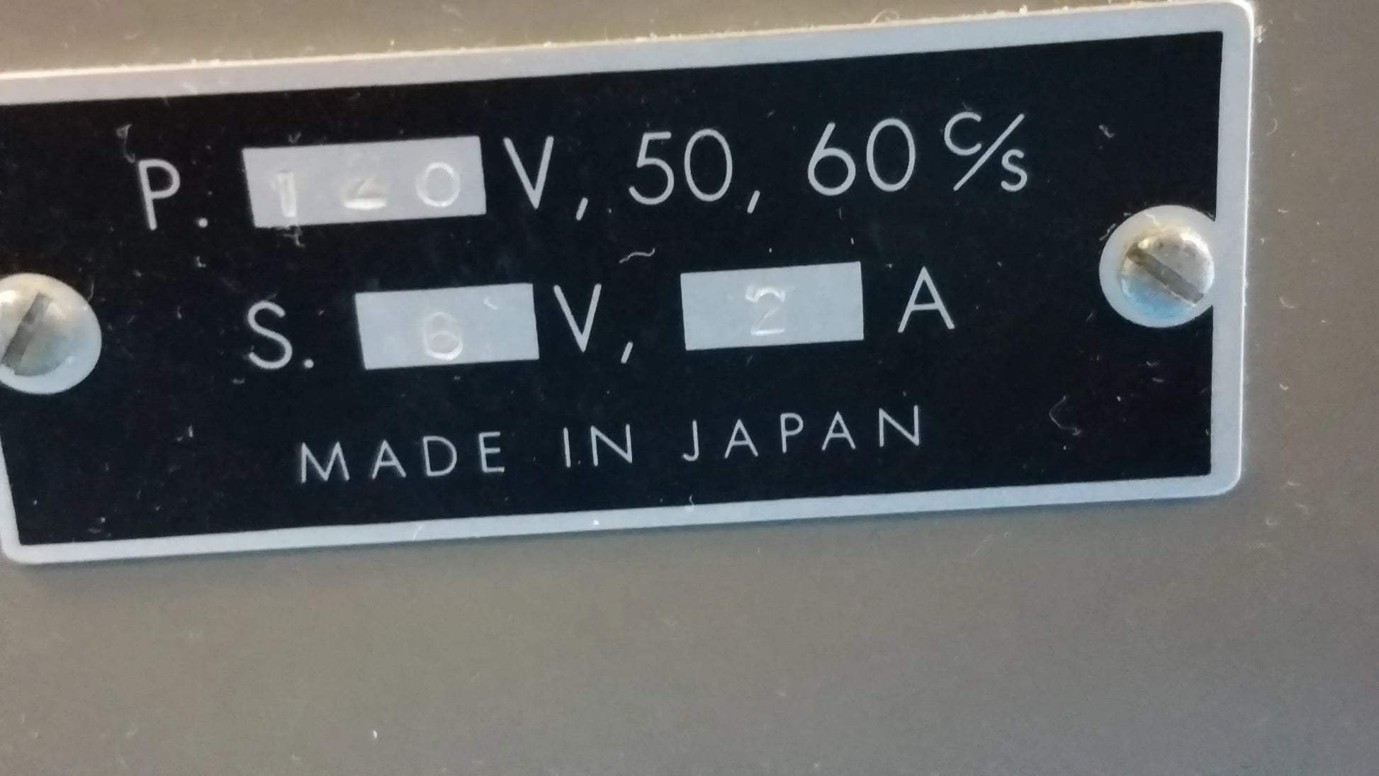 Back side of a black rectangular label with white text and silver screws on a lot of 2 stereo microscope with ck inverted binocular microscope showing electrical specifications and made in japan