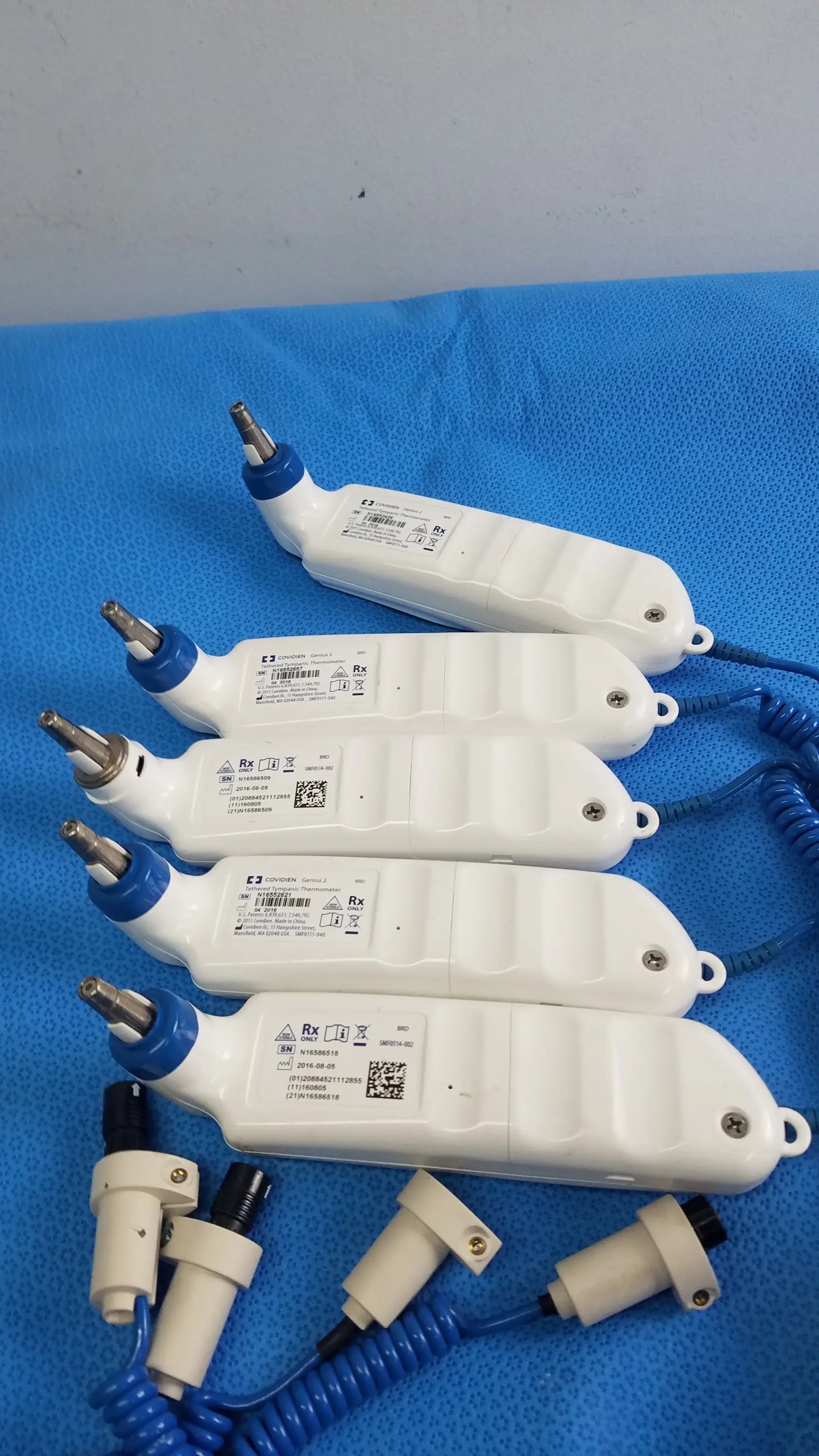 Lot of 4 coviden genius 2 tethered tympanic thermometers with white medical handpiece, blue accents, and coiled cord for reuse medical equipment