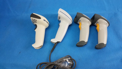 Lot of 4 white and gray laser barcode scanner readers with yellow triggers arranged on blue surface for medical equipment reuse