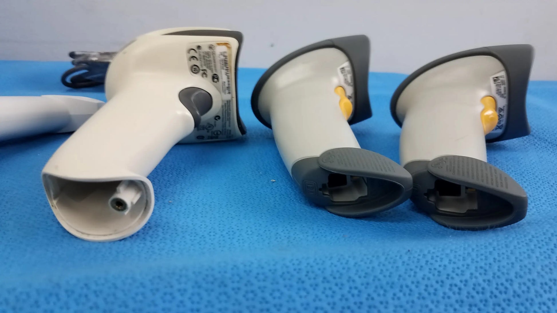 Lot of 4 laser barcode scanner readers featuring three white and gray handheld scanners with black grips and a yellow trigger button for reuse medical equipment