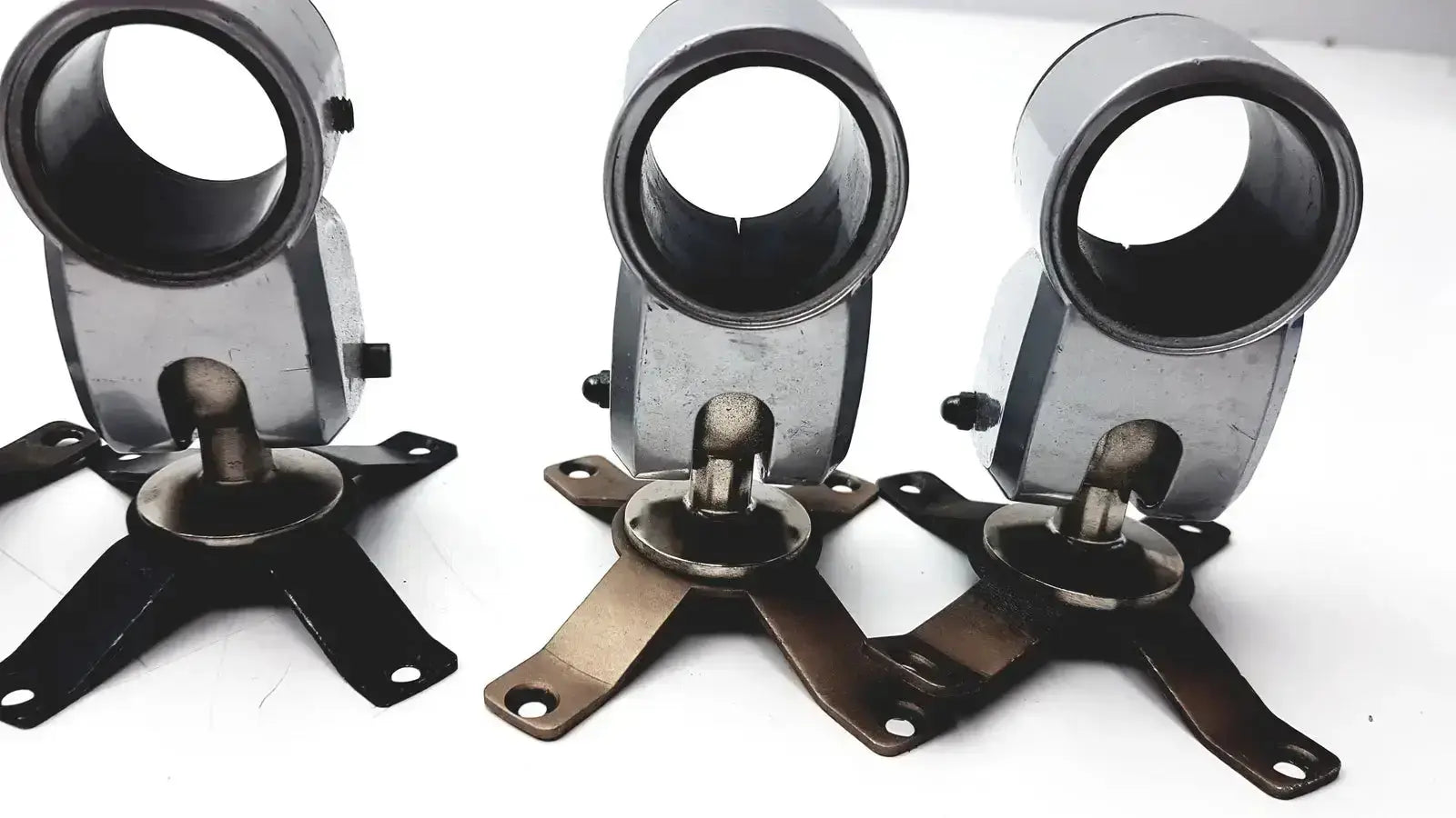 Three identical metallic metal clamps with cylindrical tops and four-legged bases for hospital surplus equipment use