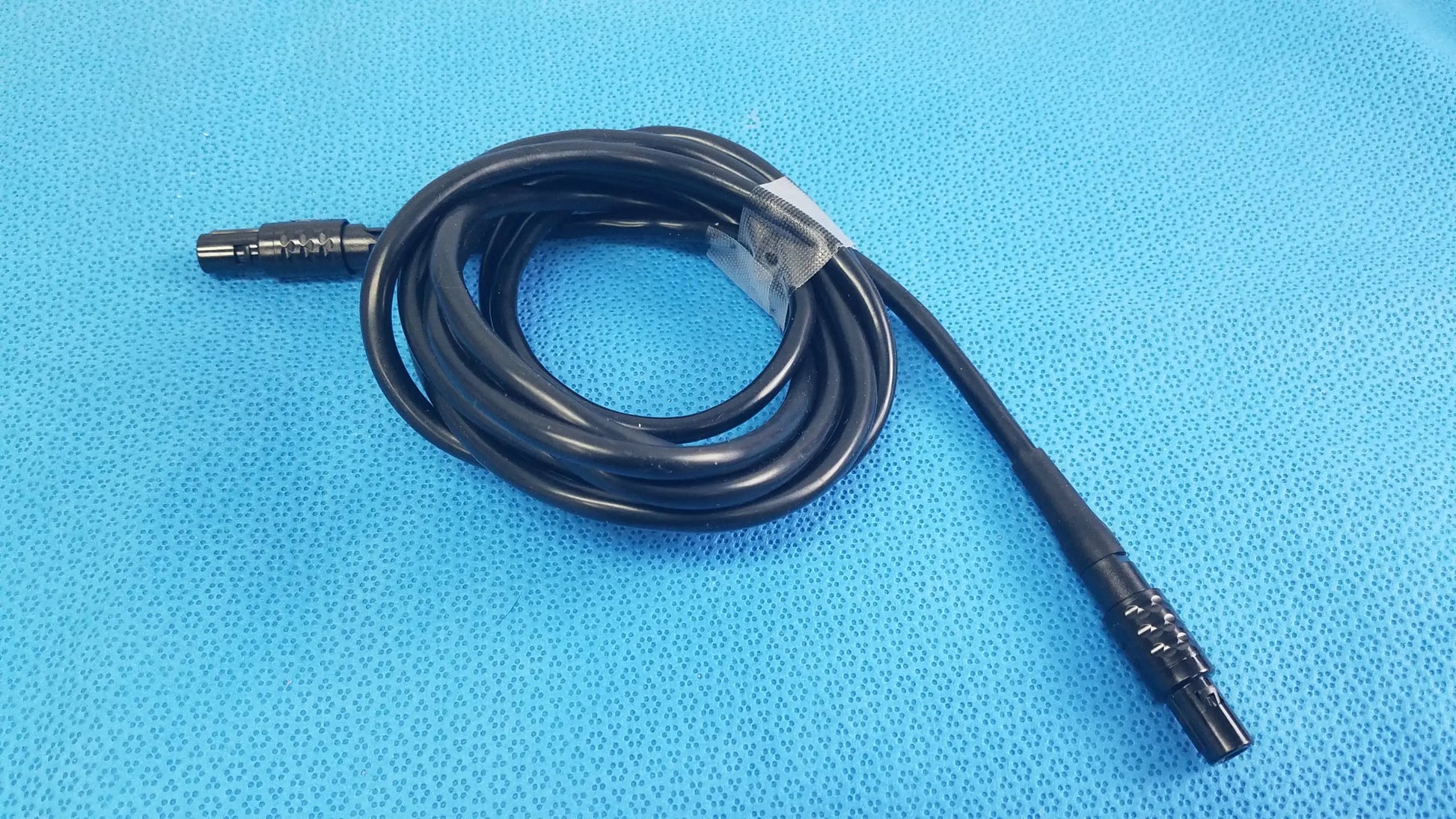 Black coiled medical surgical handpiece console extension cable with metallic connectors and clear plastic tie for medical equipment