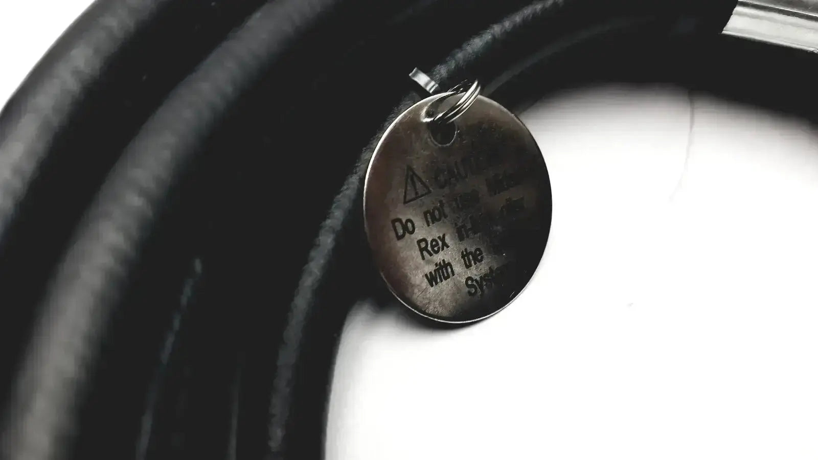 A circular metallic dog tag with warning symbol on a black collar for midas rex legend gold pneumatic device