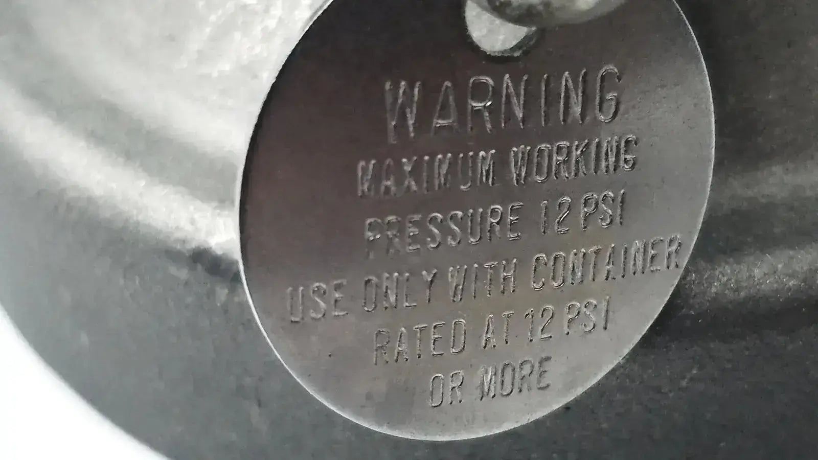 A dark metallic circular warning label with safety instructions on the back of a micro matic inlet keg coupler