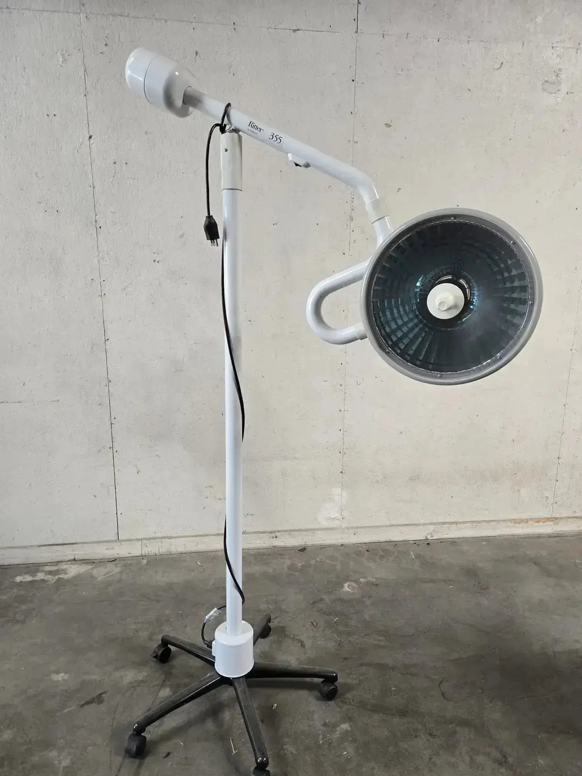 White adjustable midmark ritter surgical lamp with circular head and black wheeled base for minor surgery procedure