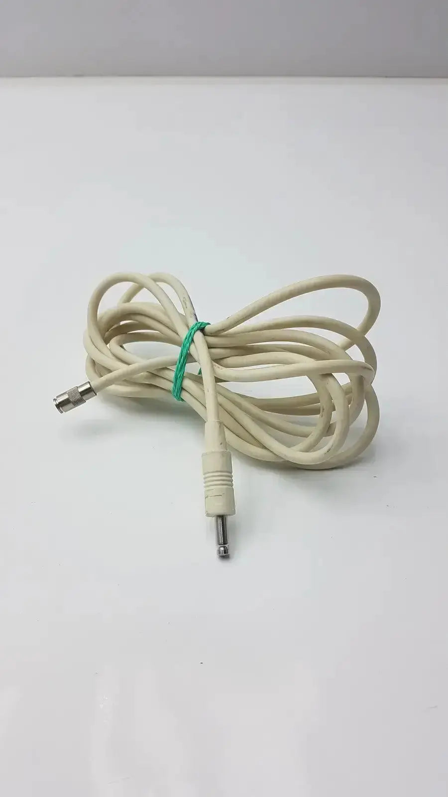 A coiled beige nbp sensor probe cable with a green tie and two metallic straight plug connectors