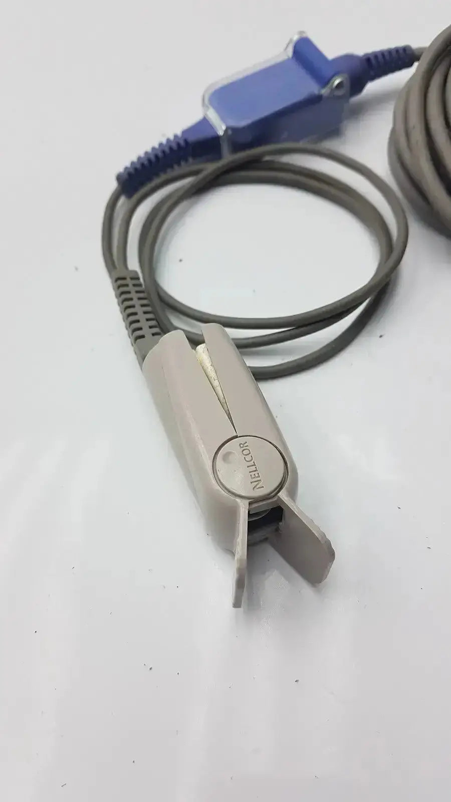Gray plastic Nellcor finger clip pulse oximeter with blue connector and coiled extension cable used medical equipment for sale