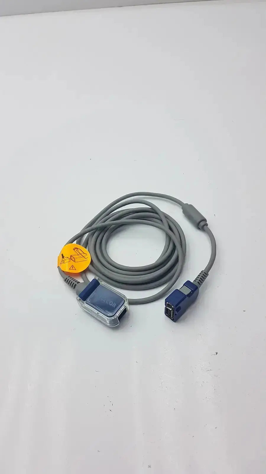 Gray coiled pulse oximetry interface cable with blue transparent sensor and orange warning label for Nellcor DOC-10