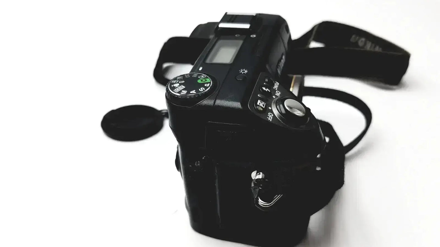 Black Nikon Coolpix E8400 digital camera with matte finish, visible dials, buttons, lens cap, reliable monitoring features
