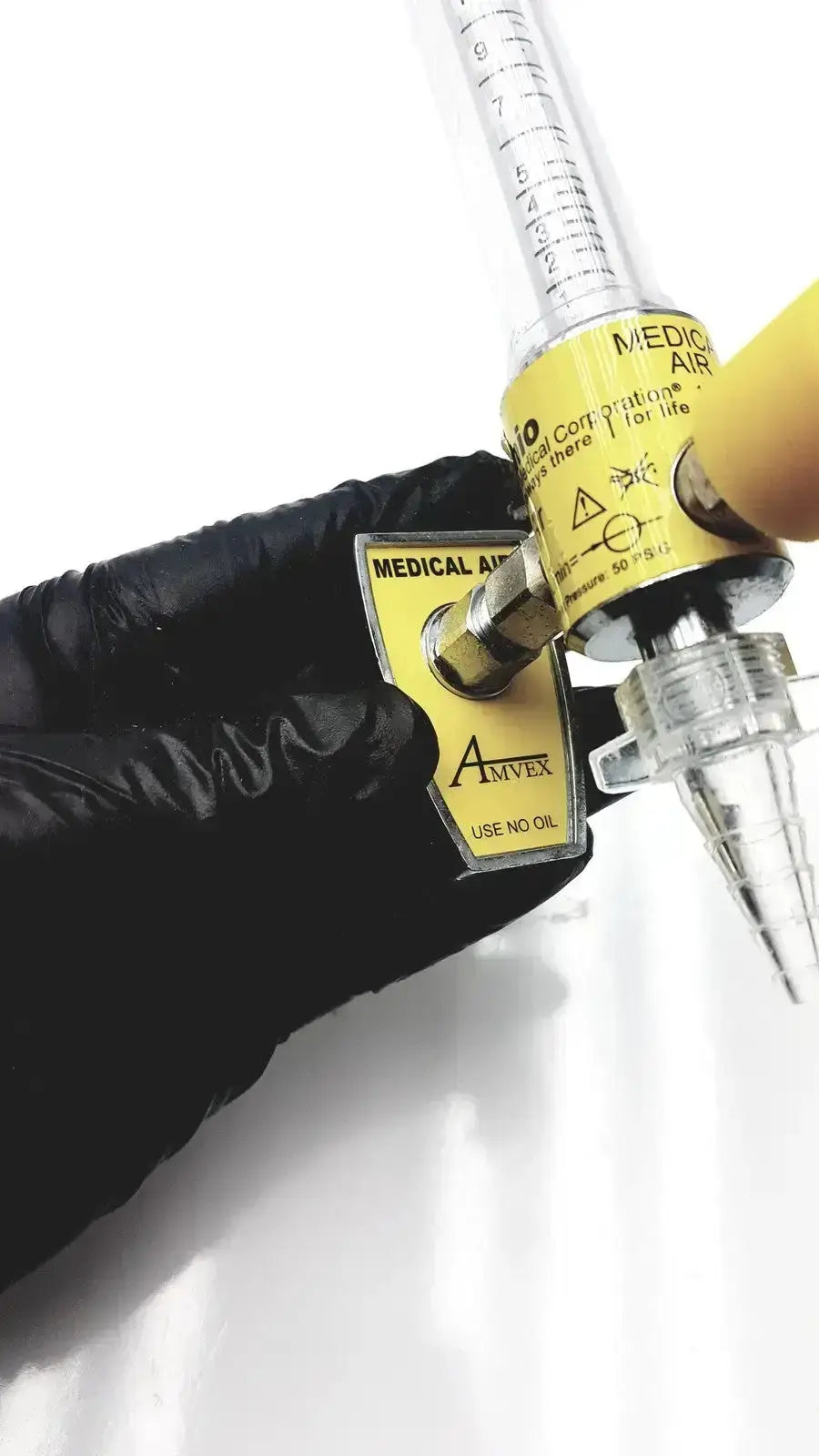 Yellow amvex medical air flow meter with clear graduated tubing held by black-gloved hand for ohio medical compressor inlet pressure 50 psig