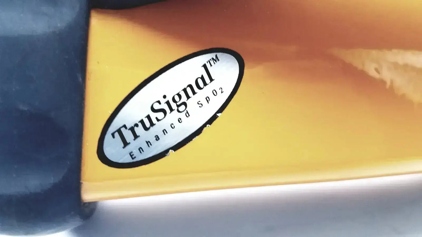 A white oval sticker with black text reading trusignal enhance spo2 affixed to a glossy orange surface of an ohmeda trusat oximeter