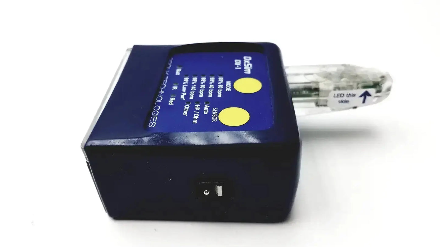 Dark blue rectangular oxsim ox-1 pulse oximeter simulator with two yellow indicators and clear led this side attachment