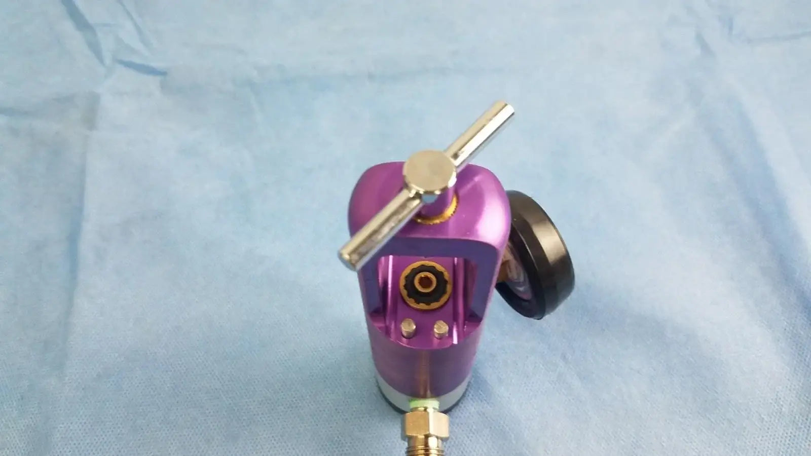 Purple metallic oxygen regulator with gold adjustment knob and black gauge for medical gas flow control device