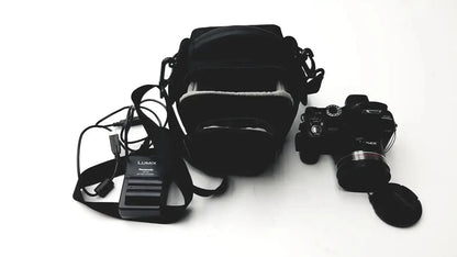 Black Panasonic model DMC-FZ35 digital camera with attached lens cap and carrying case alongside battery charger