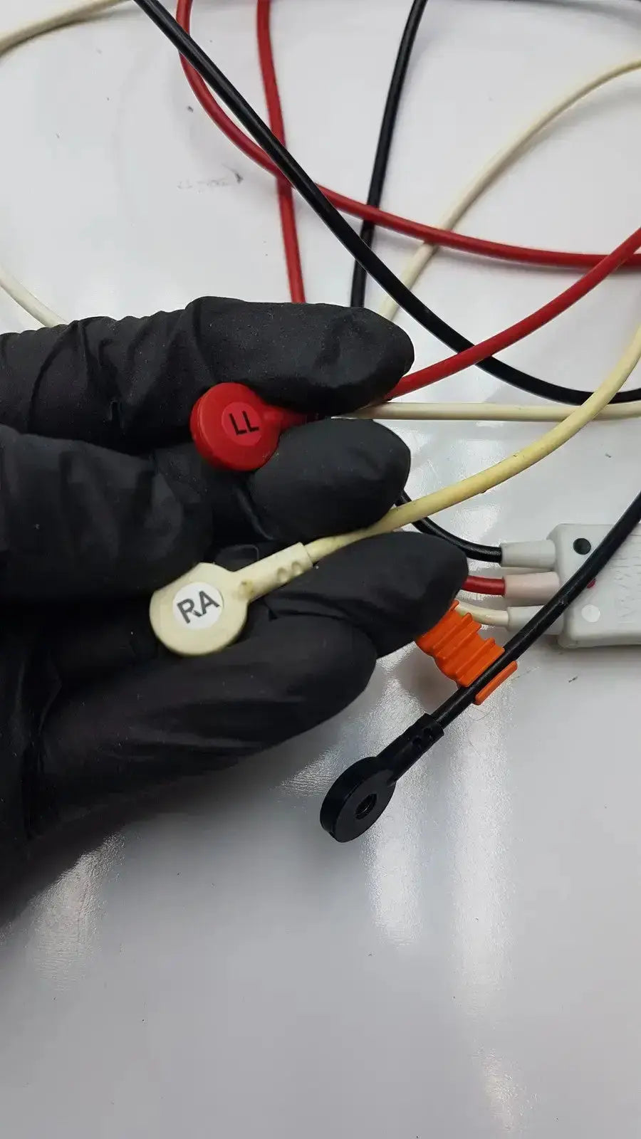 A hand in black gloves holds philips m1673a 3 leadset snap with trunk cable featuring red and beige connectors