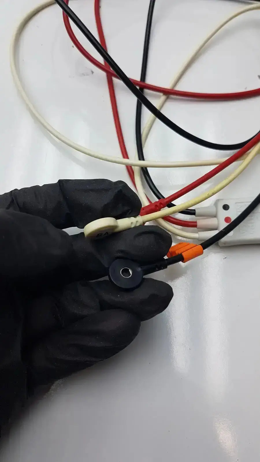 Black-gloved hand holding philips m1673a 3 leadset snap with beige and black wires and orange connectors trunk cable