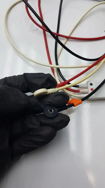 Black-gloved hand holding philips m1673a 3 leadset snap with beige and black wires and orange connectors trunk cable