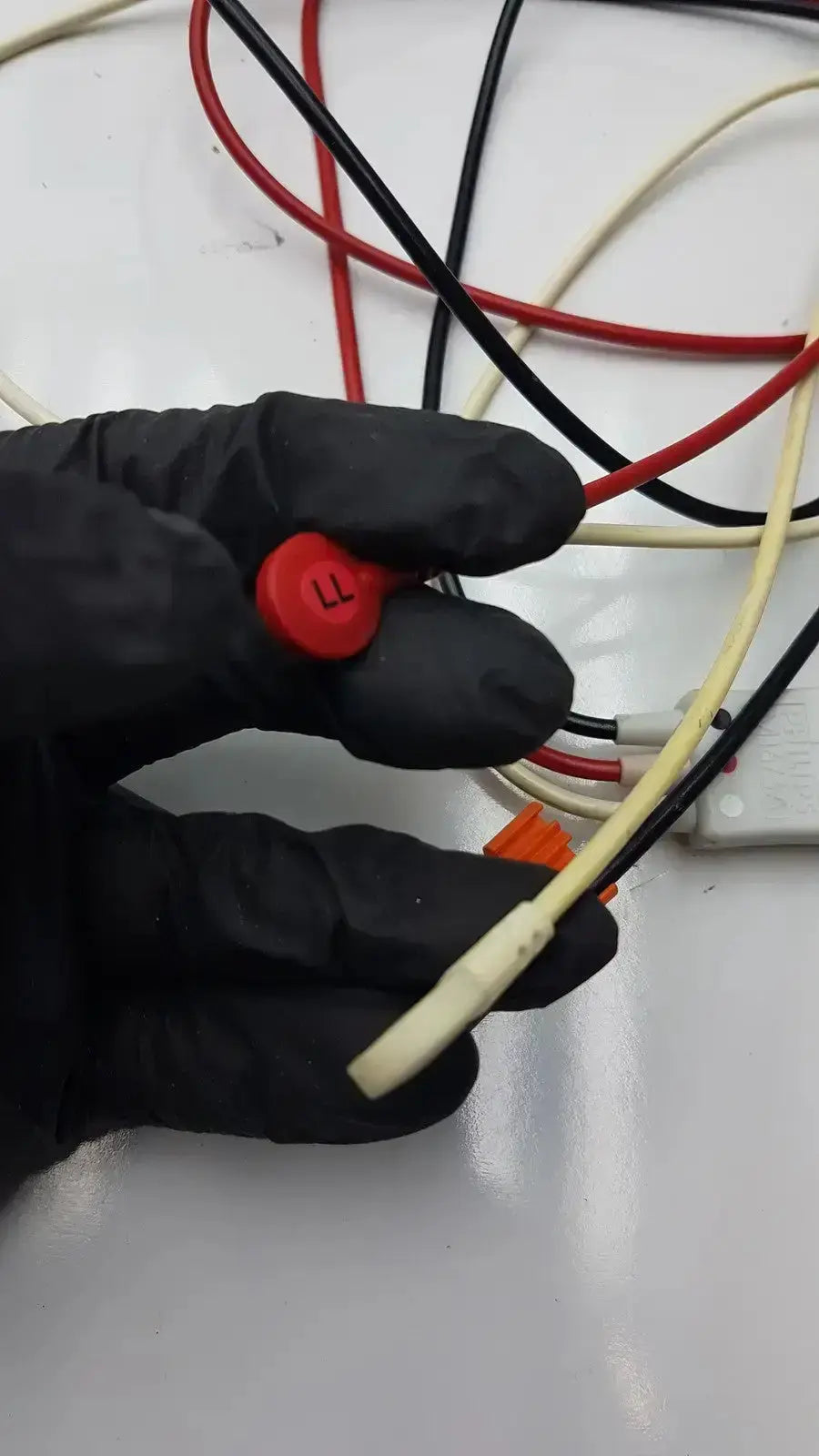 A black-gloved hand holding a red circular philips m1673a connector labeled ll with a trunk cable and multicolored wires