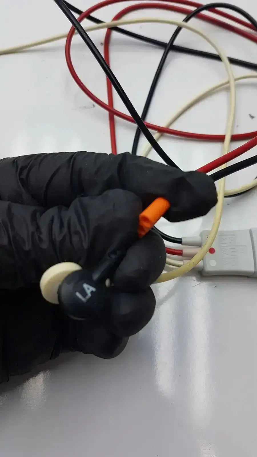 Black-gloved hand holding orange electrical connector with trunk cable and white la label on philips m1673a leadset