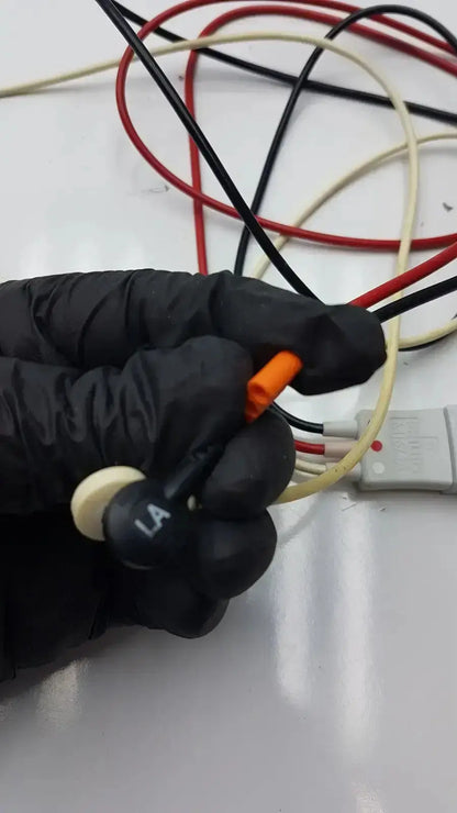Black-gloved hand holding orange electrical connector with trunk cable and white la label on philips m1673a leadset