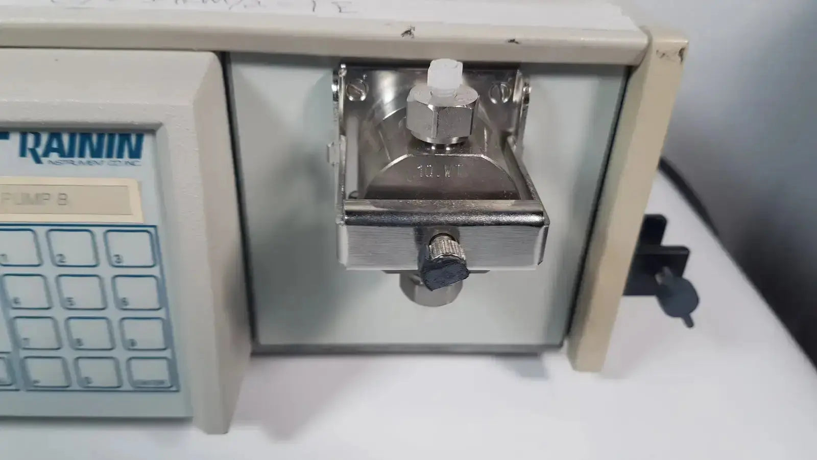 Silver metallic pump head with hexagonal knob and white cap mounted on beige rainin hpxl solvent delivery system