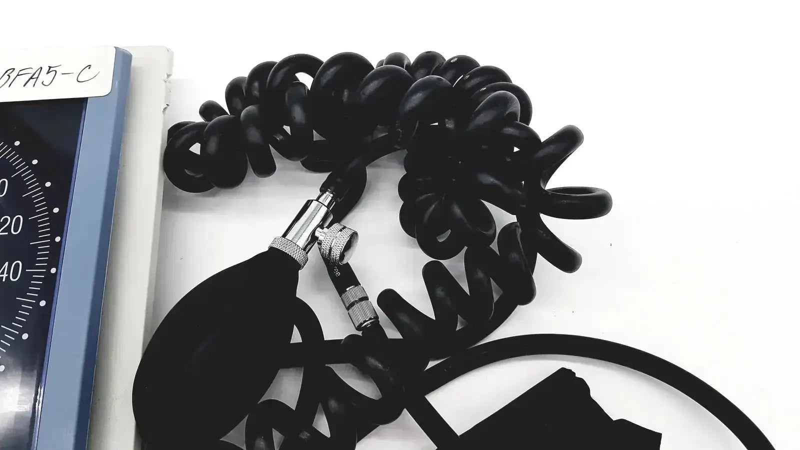 Black coiled rubber tubing with metallic connectors and bulbous inflation chamber of riester big ben square sphygmomanometer