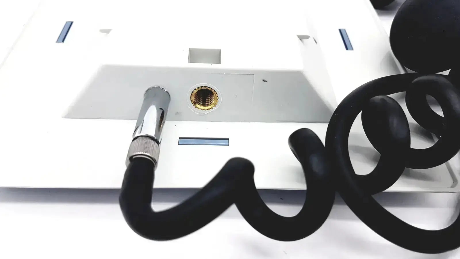 Black coiled telephone cord with metallic connector attached to white riester big ben square sphygmomanometer device