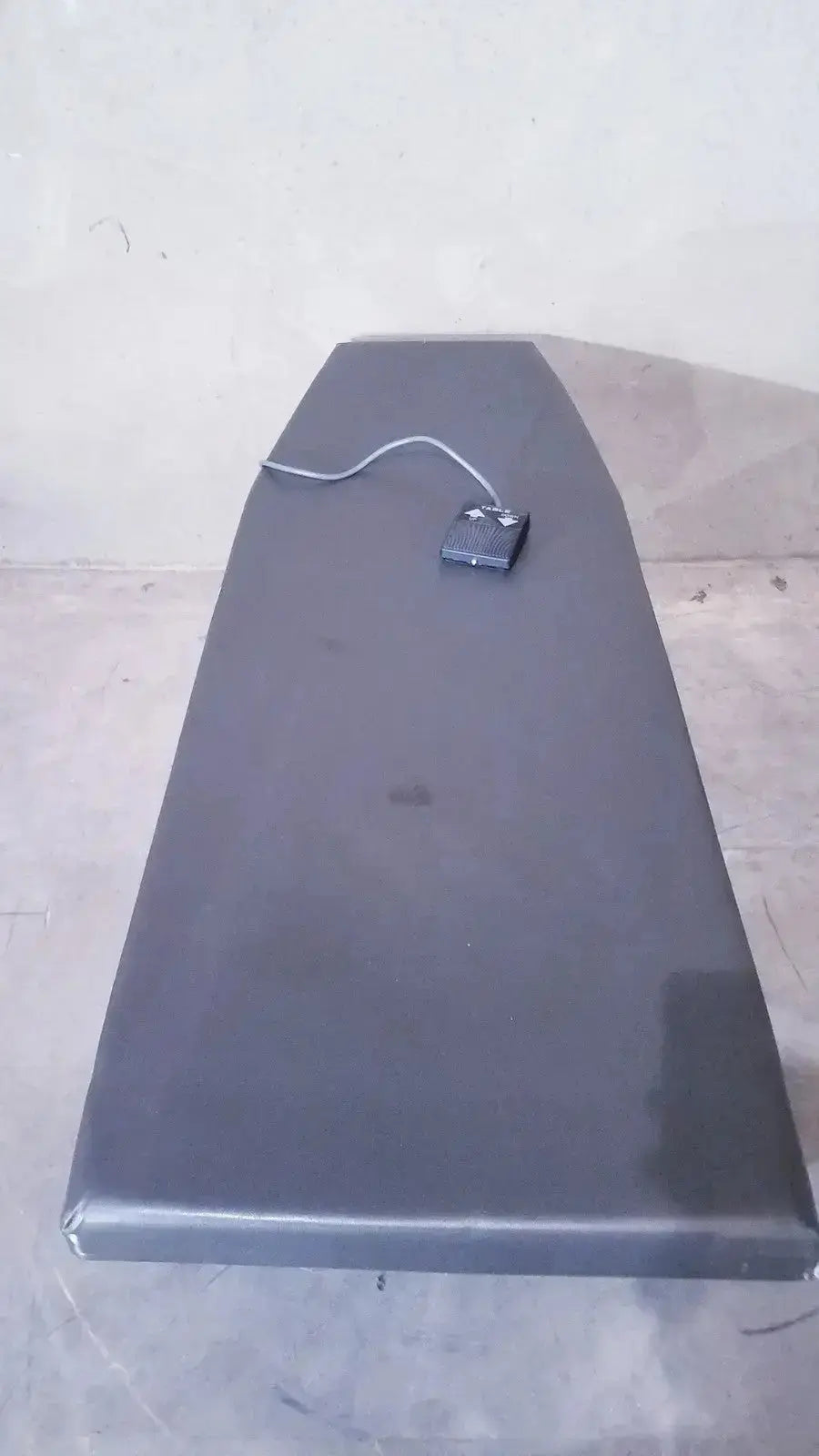 Black ironing board exam table with matching foot paddle and cord for hospital surplus use