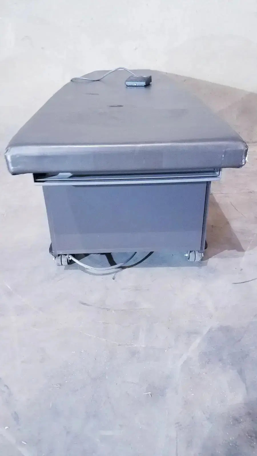 Gray padded Ritter 106 exam table with metal frame, caster wheels, and up and down foot paddle for hospital surplus