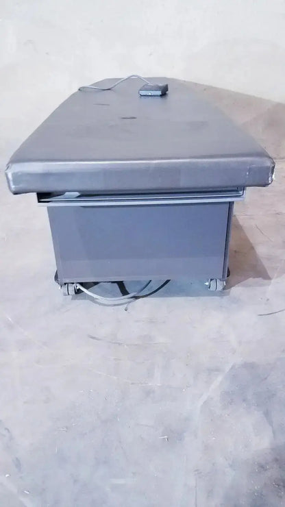 Gray padded Ritter 106 exam table with metal frame, caster wheels, and up and down foot paddle for hospital surplus