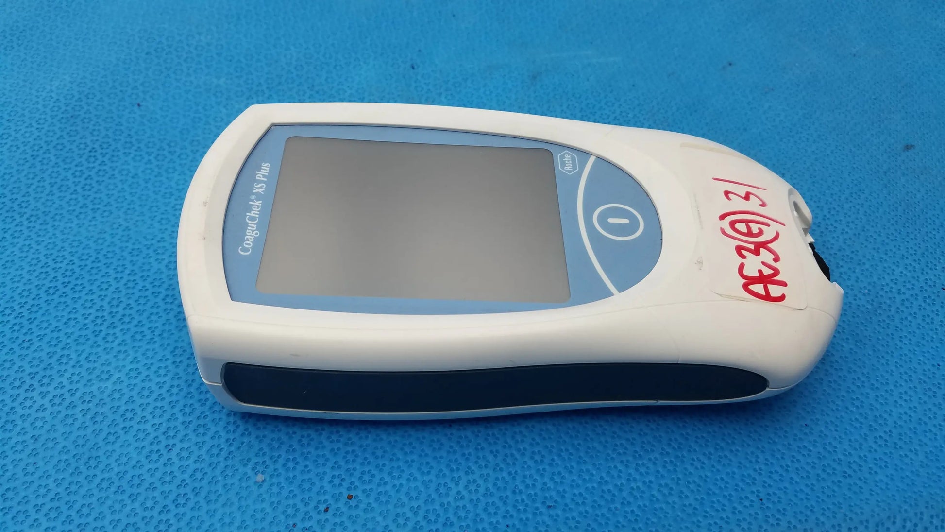 Roche coaguchek xs plus handheld medical equipment with white and blue body, rectangular screen, and circular button on right side