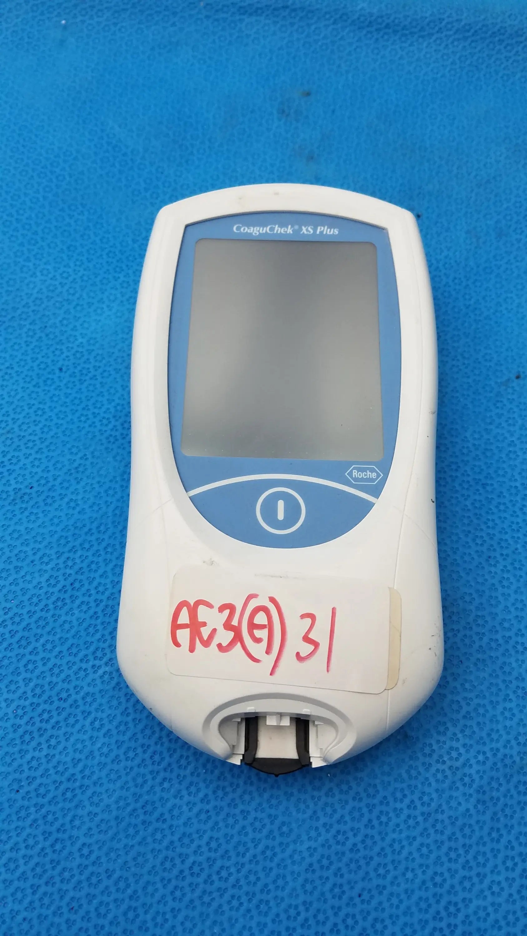 White and blue roche coaguchek xs plus coagulation meter with small screen, circular button, and bottom test strip slot medical equipment
