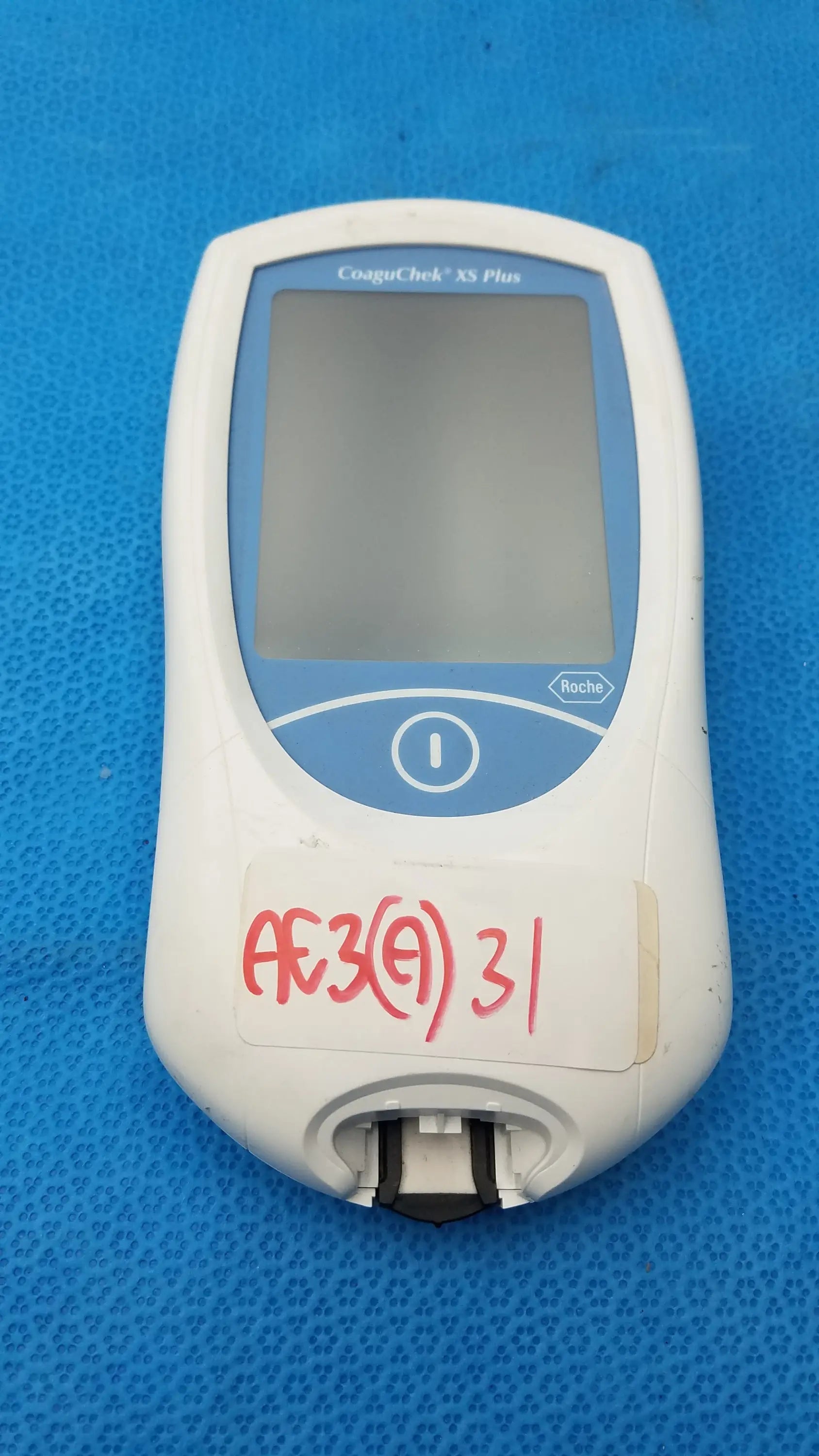 White and blue Roche CoaguChek XS Plus medical equipment with rectangular screen and circular button for coagulation testing