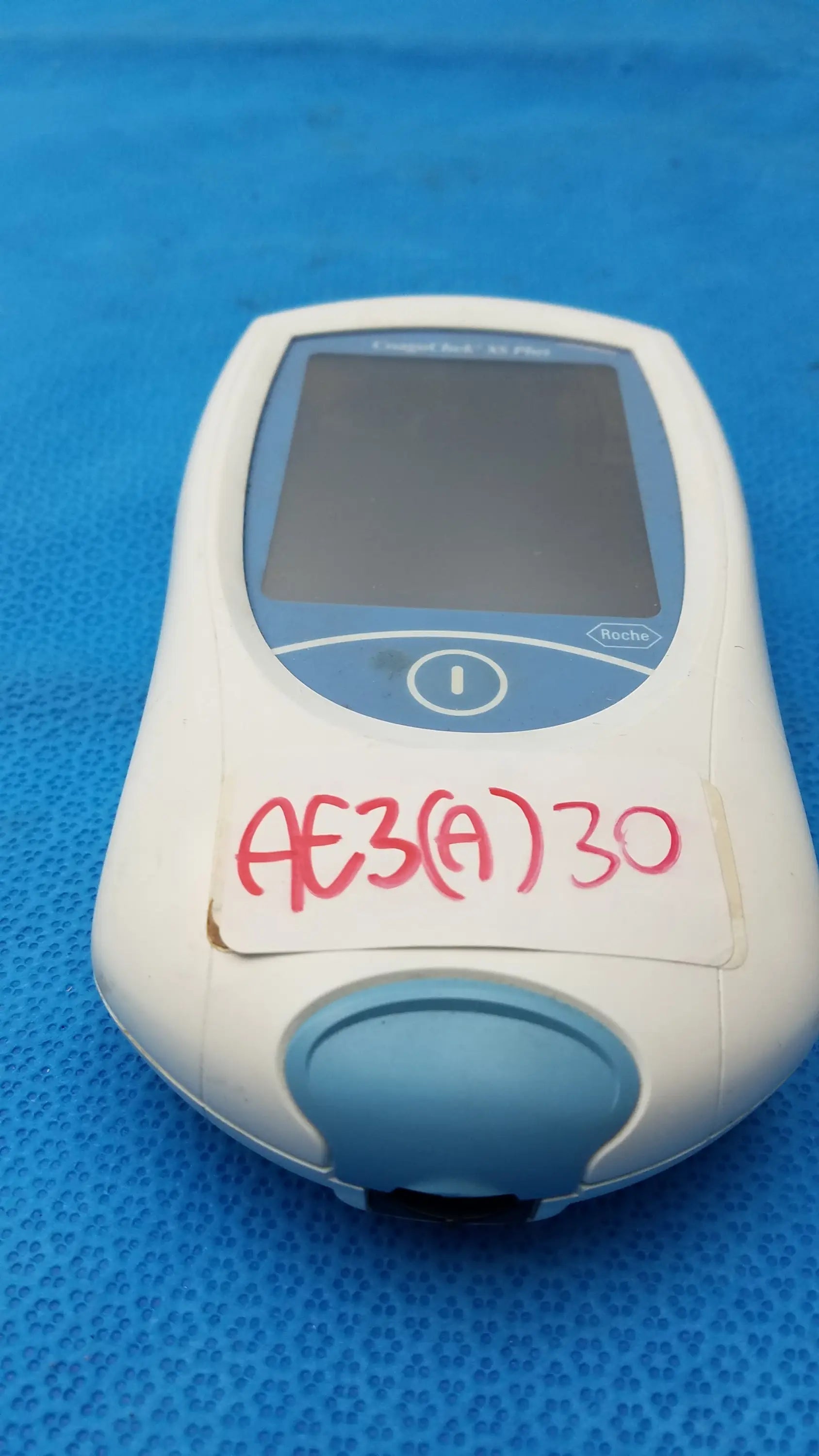 Roche coaguchek xs plus coagulation meter in white and light blue with small screen circular button and red handwritten label