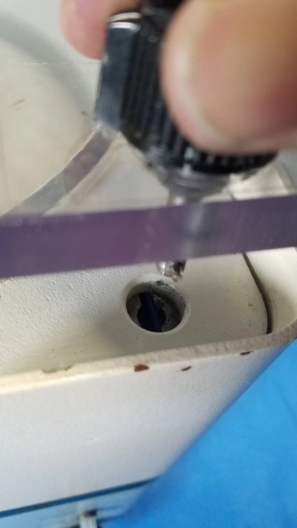 A hand holds a black textured screwdriver with metallic tip above an old white sewing machine near savant hsc 10k-115 high speed centrifuge for reuse medical equipment