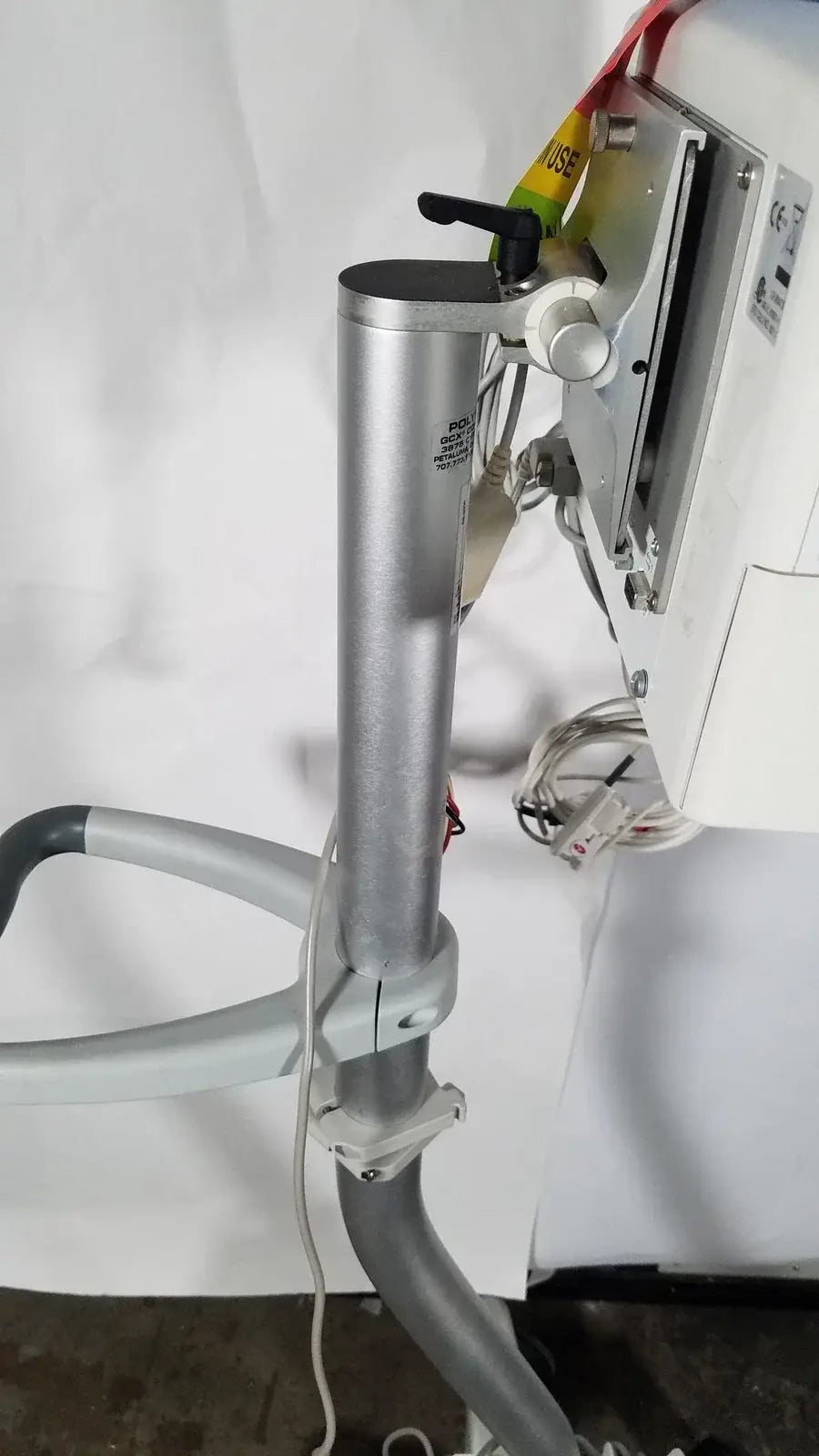 Silver cylindrical metal pole with black handle and white knob mounted on gray articulated arm of spacelabs patient monitor rolling stand medical equipment
